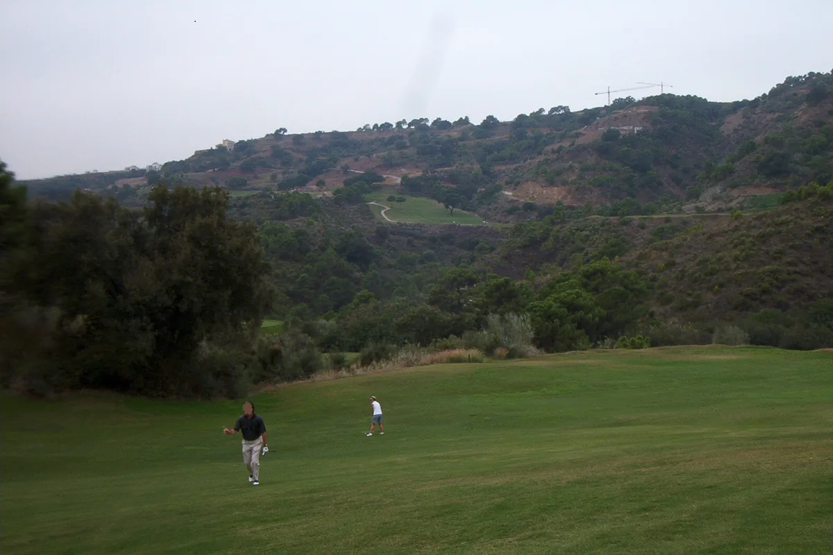 Players walking on a fairway below wooded hillsides on a golf course in Benahavís