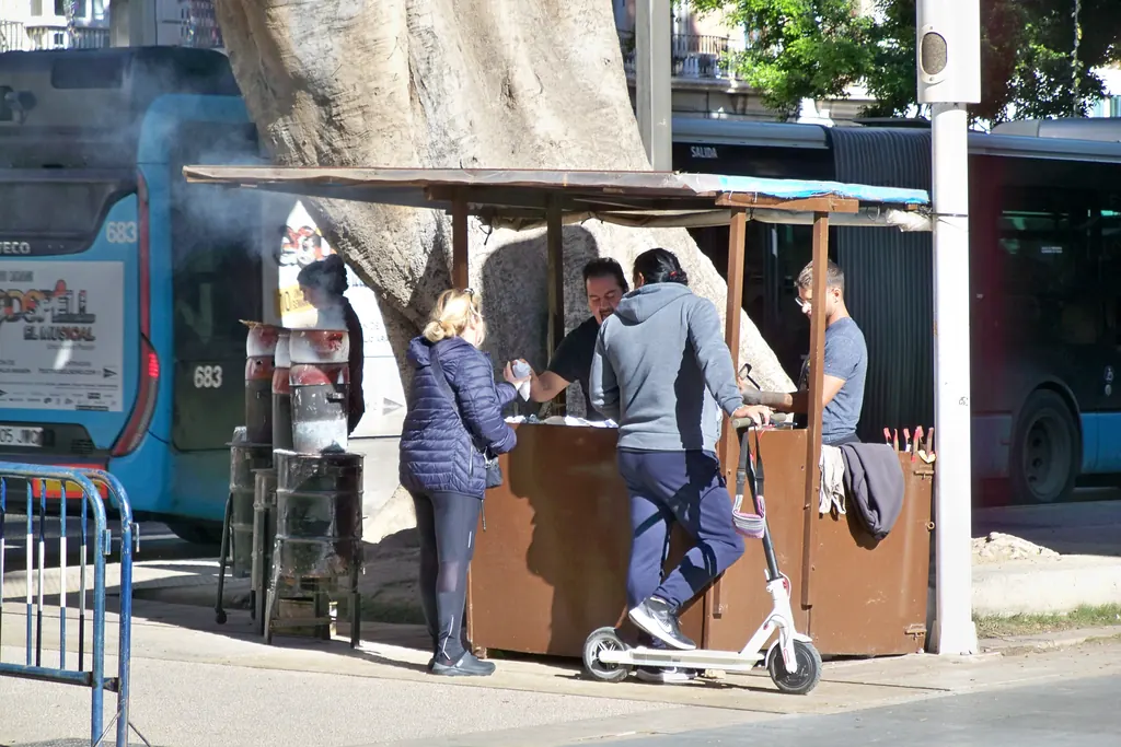 Street food stall on the Alameda Principal in Málaga with customers buying roasted chestnuts