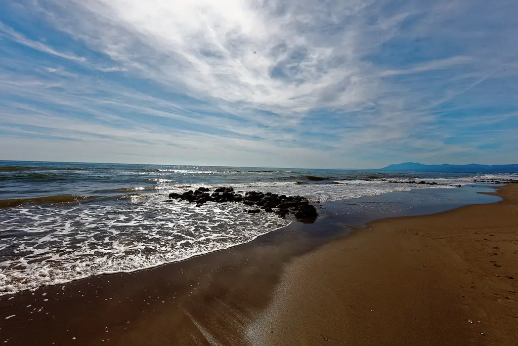 Playa de las Chapas beach in Elviria, Marbella East, with dark rocks at the water's edge and the coastline stretching west