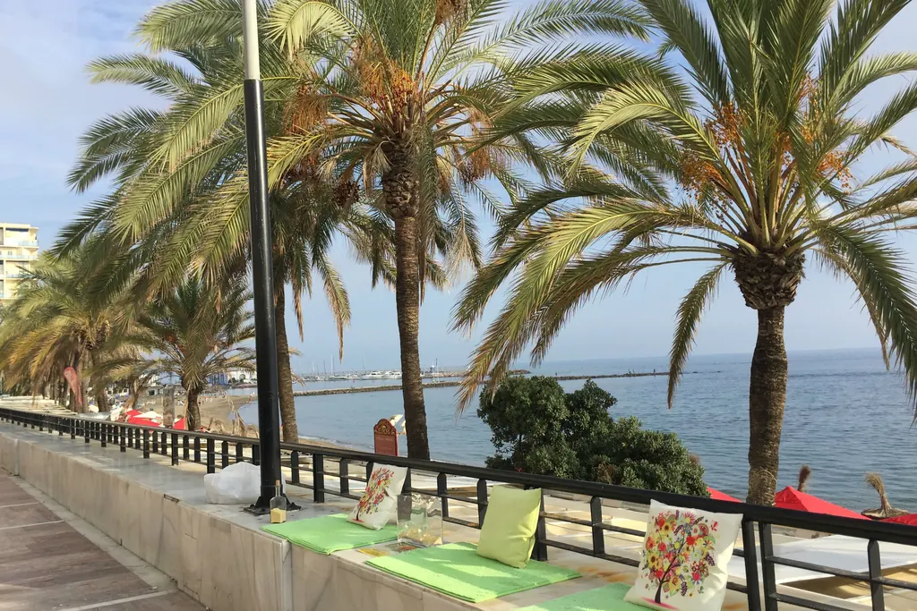 Palm-lined seafront walkway in Marbella with a market stall and the Mediterranean beyond