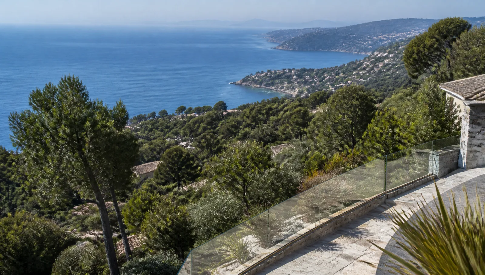 Elevated stone terrace with glass balustrade looking over wooded hillside towards the Mediterranean coastline