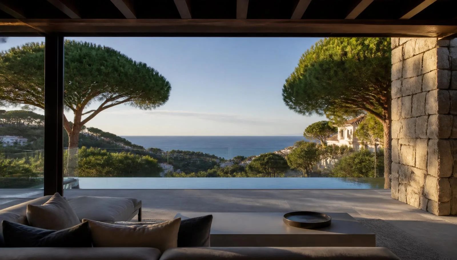 View from a covered terrace of a hillside home across an infinity pool and umbrella pines towards the Mediterranean sea in the distance