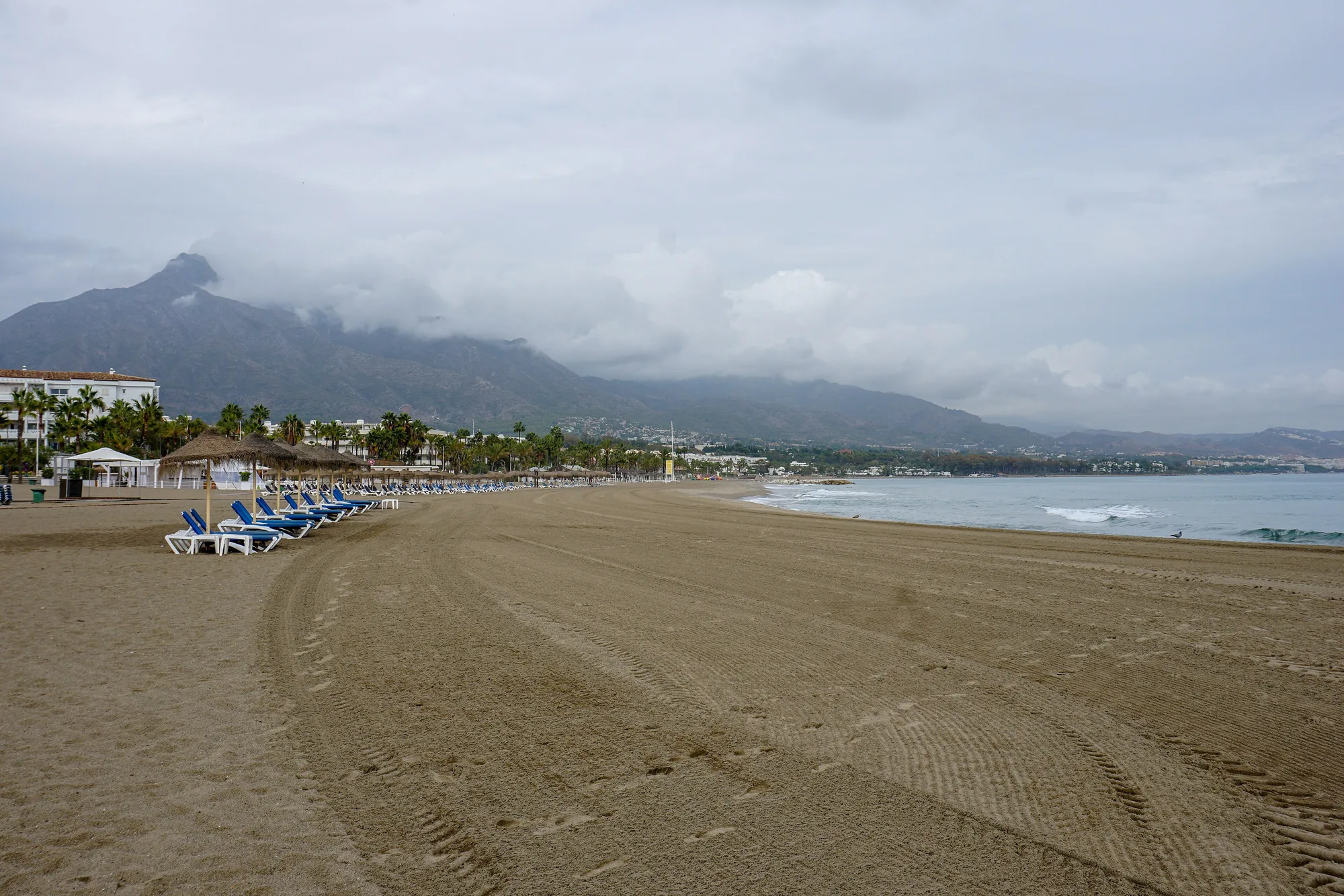 Wide sandy beach beside Puerto Banús in Marbella, with the coastline and mountains behind it